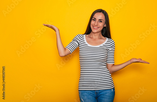 Beautiful smiling modern brunette woman in casual wear is posing against yellow wall