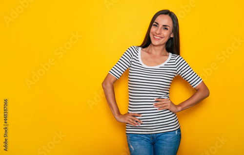 Beautiful smiling modern brunette woman in casual wear is posing against yellow wall