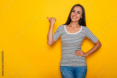 Beautiful smiling modern brunette woman in casual wear is posing against yellow wall