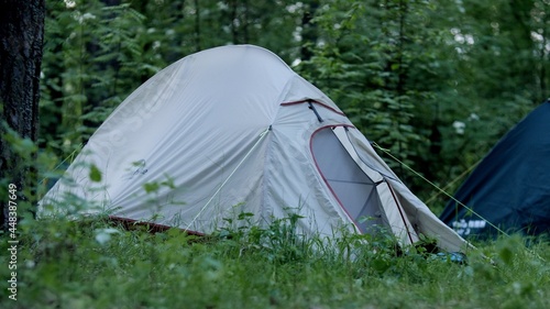 Empty camping white tent in the forest on a cloudy day. Summer day, many trees and green grass. Tourism concept. Hike, extreme conditions. Camping equipment for long trips