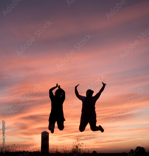 The image of people jumping over the beautiful colorful sky in the evening.