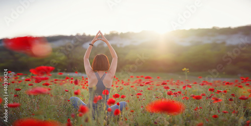 Photography A beautiful woman meditates on a poppy field at sunset