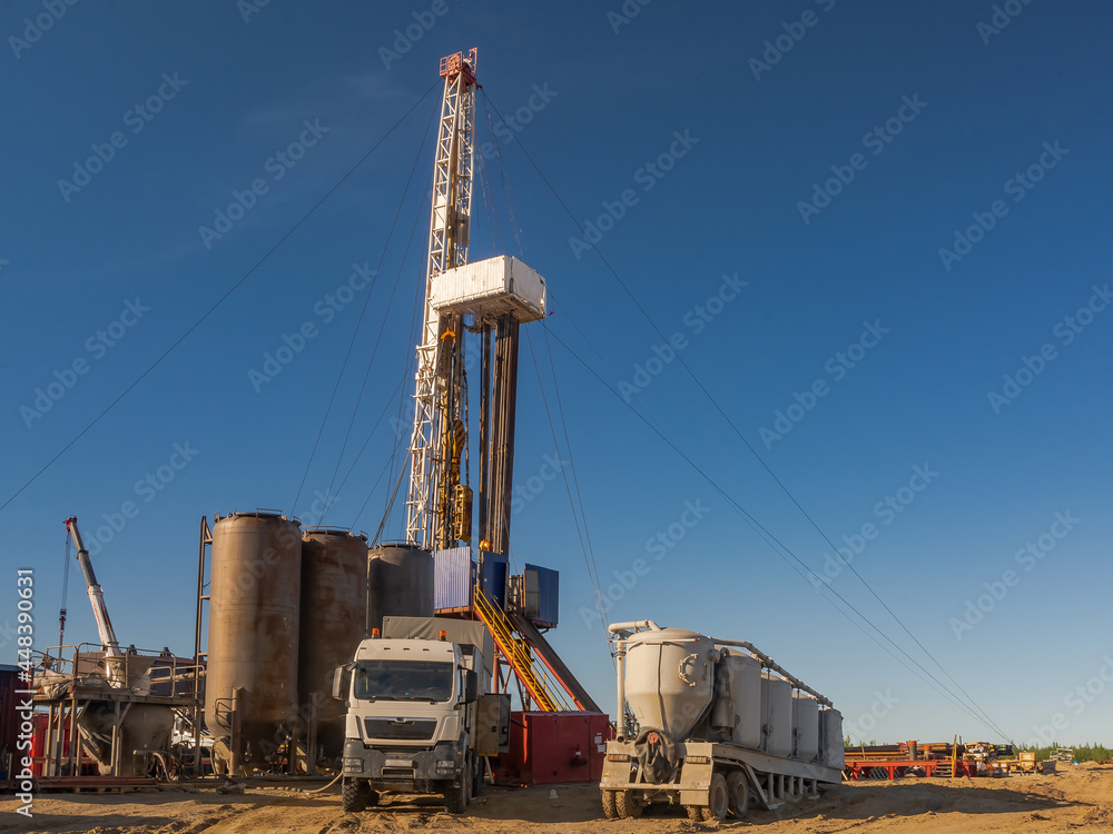 Drilling rig with well cementing equipment in the foreground. Infrastructure, communications and drilling equipment are visible. Cementing unit on a car chassis. Cement storage tanks