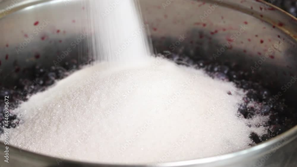 A woman pours sugar into a container with blueberries. Making blueberry jam at home. Preservation and preparation of blueberries. Close-up shot. A woman pours sugar into a container with blueberries. Making blueberry jam at home. Preservation and preparation of blueberries. Close-up shot.