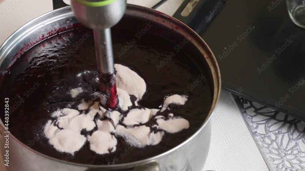 A woman adds agar agar to blueberry and sugar puree. Mixes them with a blender. Making blueberry jam at home. Preservation and preparation of blueberries. Close-up shot. A woman adds agar agar to blueberry and sugar puree. Mixes them with a blender. Making blueberry jam at home. Preservation and preparation of blueberries. Close-up shot.