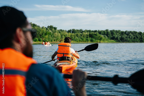 People in orange life jackets kayaking on a big wide river. © zzzdim