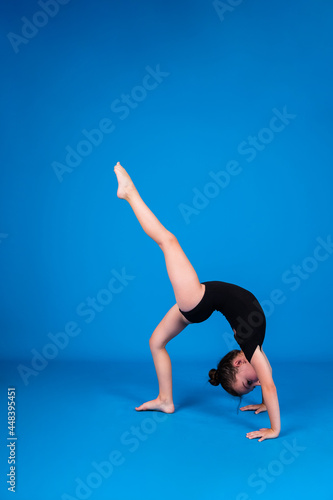 an elegant little gymnast performs a balance exercise on a blue background with a place for text