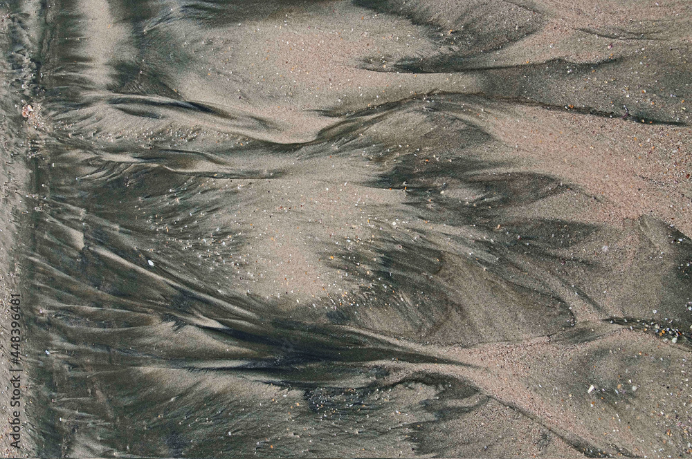 Water creates a distinctive pattern in the sand of a beach with shell ...