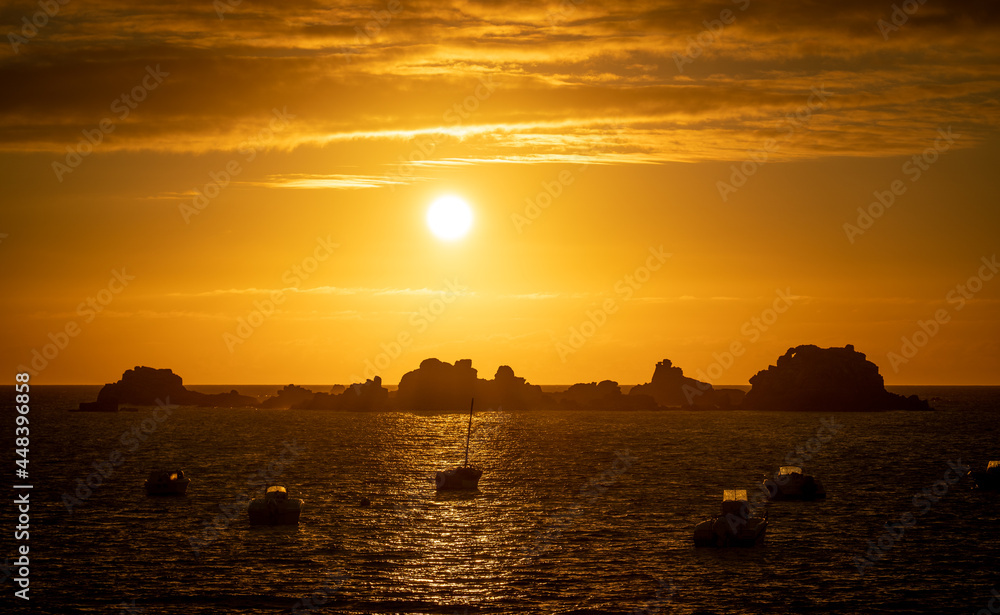 Fototapeta premium Blick von der Atlantikküste bei Plougrescant auf die zerklüfteten Felsen und Fischerboote im Sonnenuntergang, Bretagne, Frankreich