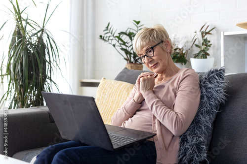 An older woman with short blonde hair sits on sofa in living room and chats with her children on laptop over video chat during lockdown