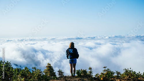 
Young girl on top of a mountain peak gazing at the views over a blanket of clouds. Alone in the middle of nature, with the feeling of purity, peace and tranquility, of disconnection with the world. L