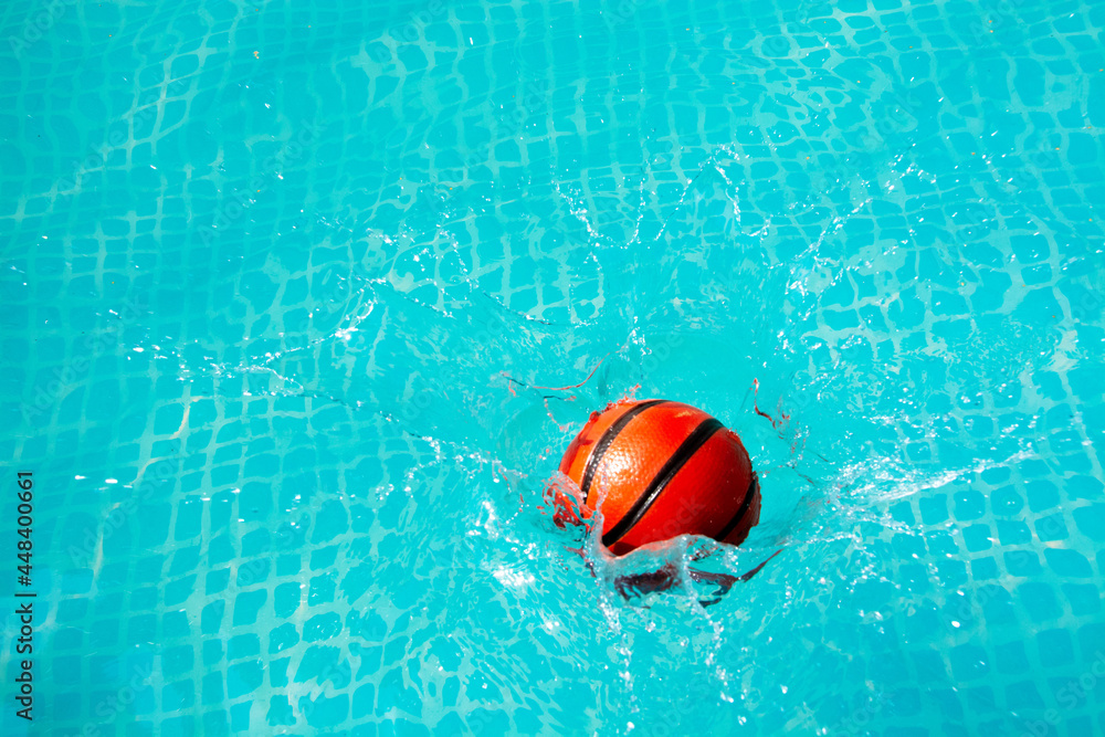 Ball drop on blue surface swimming water. Basketball in the pool. Summer concept for play and refreshment.
