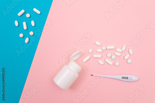 White Pills or Tablets Scattered from the Pill Container with Electronic Thermometer on Split Pink and Blue Background. Pharmaceutical Industry and Medicinal Products