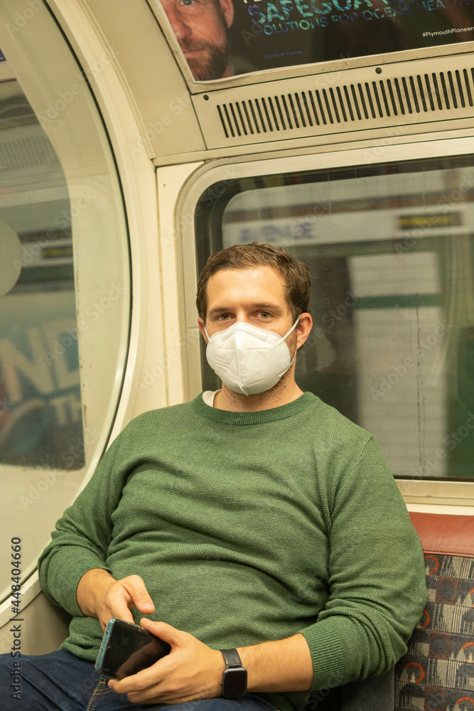 London UK - August 1st 2021: Young guy wearing a face mask in London Underground checking his phone