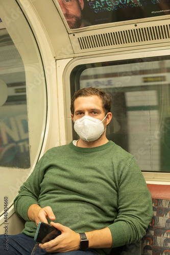 Obraz na płótnie London UK - August 1st 2021: Young guy wearing a face mask in London Underground checking his phone w salonie