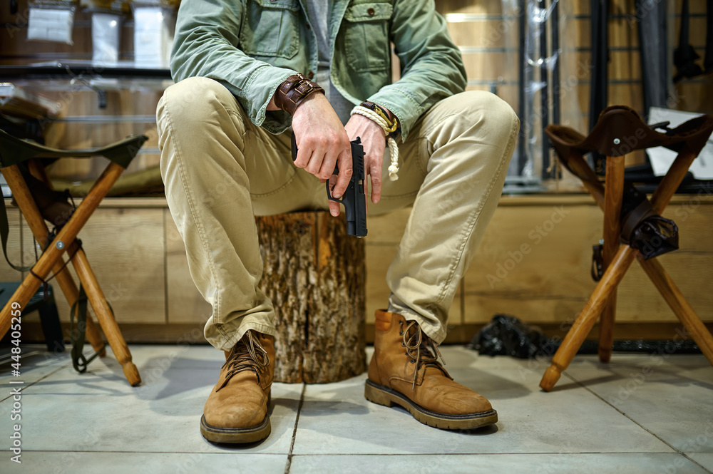Man with pistol sitting on stump in gun store Man with pistol sitting on stump in gun store