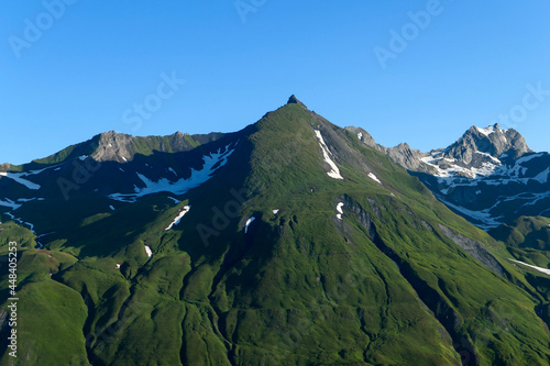 View of green mountains with pastures. Snowcapped peaks in the background.