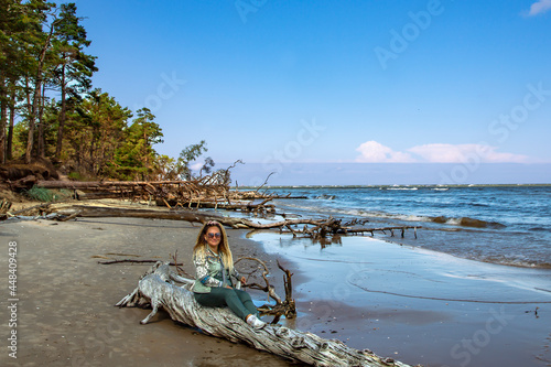 A cute woman with curly hair sits on the trees that have fallen after a storm on the shore of the Baltic Sea. Cape Kolka, Latvia photo