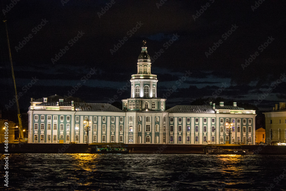 Saint Petersburg, Russia, July, 20, 2021: frontal view of the historical palace-museum of the Kunstkamera with evening illumination and the Neva River against the black night sky
