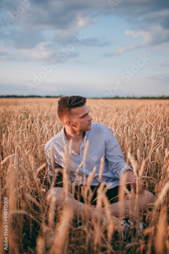 a village guy is sitting in a field in a white shirt and enjoying nature