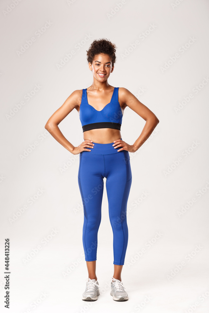 Full length of confident athletic african-american girl in sportswear,  smiling pleased, holding hands on waist with determined expression, workout  over white background Stock Photo | Adobe Stock