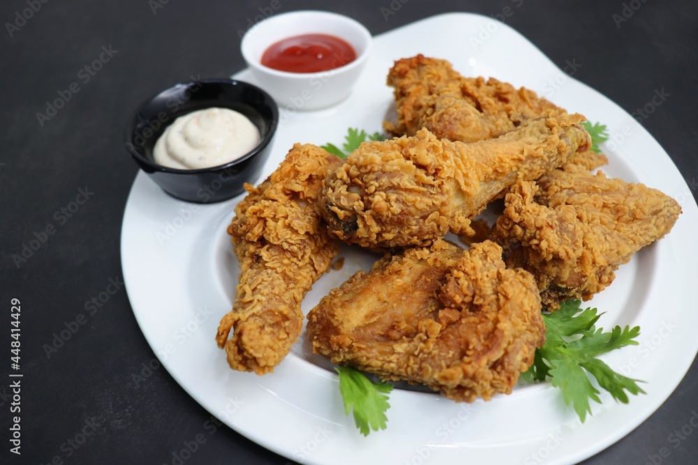 Fresh, hot, crispy deep fried chicken served on a white plate with tomato ketchup and mayonnaise. Chicken snack, hot fried chicken wings. Fast food over moody dark black background with copy space. Fresh, hot, crispy deep fried chicken served on a white plate with tomato ketchup and mayonnaise. Chicken snack, hot fried chicken wings. Fast food over moody dark black background with copy space.