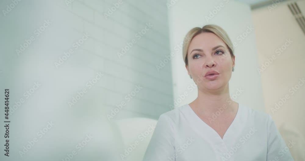 A close-up female cosmetologist is sitting in the cosmetology room and talking with somebody in front of her. A close-up female cosmetologist is sitting in the cosmetology room and talking with somebody in front of her.