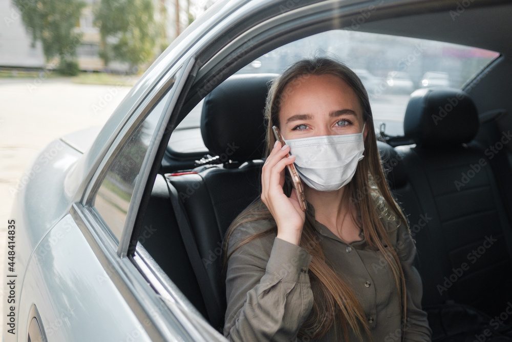 A beautiful young girl in a mask sits in the car, looks into the frame and talks on the phone. Protective mask against coronavirus. A beautiful young girl in a mask sits in the car, looks into the frame and talks on the phone. Protective mask against coronavirus.