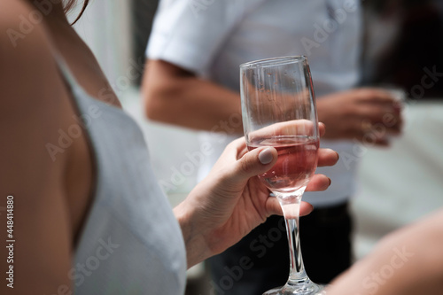 Close-up of a female hand holding a glass of pink champagne at a party.