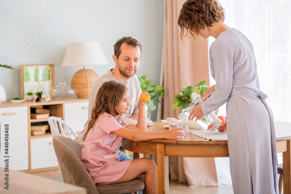 Happy family together at table. Mom pours water into daughter's glass. Happy family together at table. Mom pours water into daughter's glass.