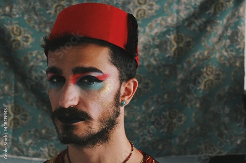 Portrait of queer young man with full face drag makeup & turkish anatolian ottoman traditional clothing with authentic patterns background *4