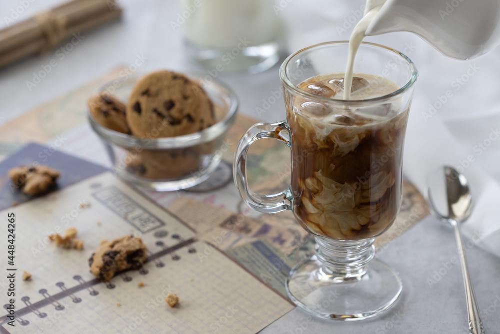 Iced coffee with milk pouring from saucer and chocolate chips cookies Iced coffee with milk pouring from saucer and chocolate chips cookies