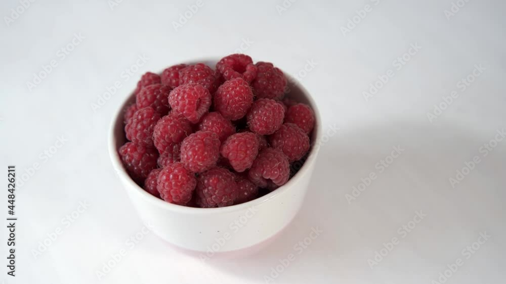 Delicious raspberries in a white plate. Fresh harvest of ripe berries. The plate spins around. White background, top view. Delicious raspberries in a white plate. Fresh harvest of ripe berries. The plate spins around. White background, top view.