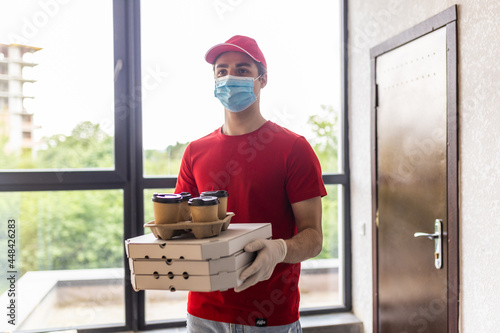 Portrait of delivery man in uniform with cardboard brown and white boxes and take away coffee cups delivering breakfast to a customer's home.