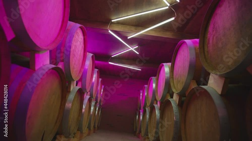 Aged Wooden Barrels With A Wine , Brandy or Whiskey In A Big Warehouse . Dolly , ronin movemant a long row of wine barrels at a colorful winery with strobe lights .  photo