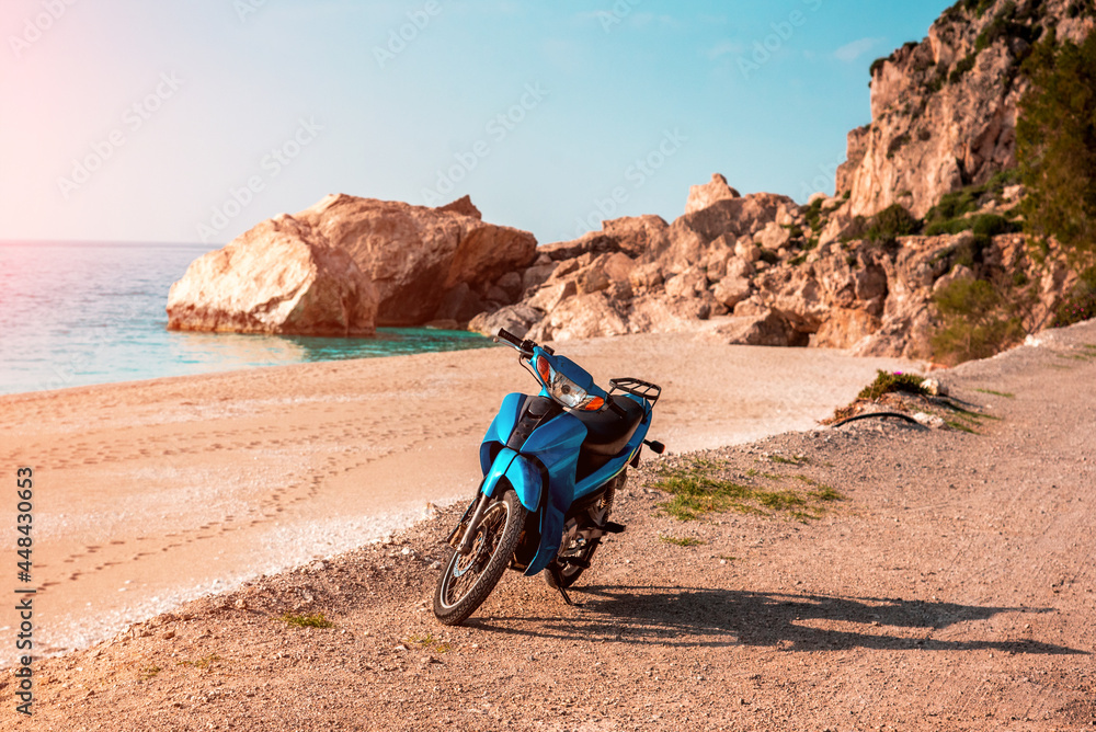 Summer landscape with a blue scooter by the sea on a background of rocks.