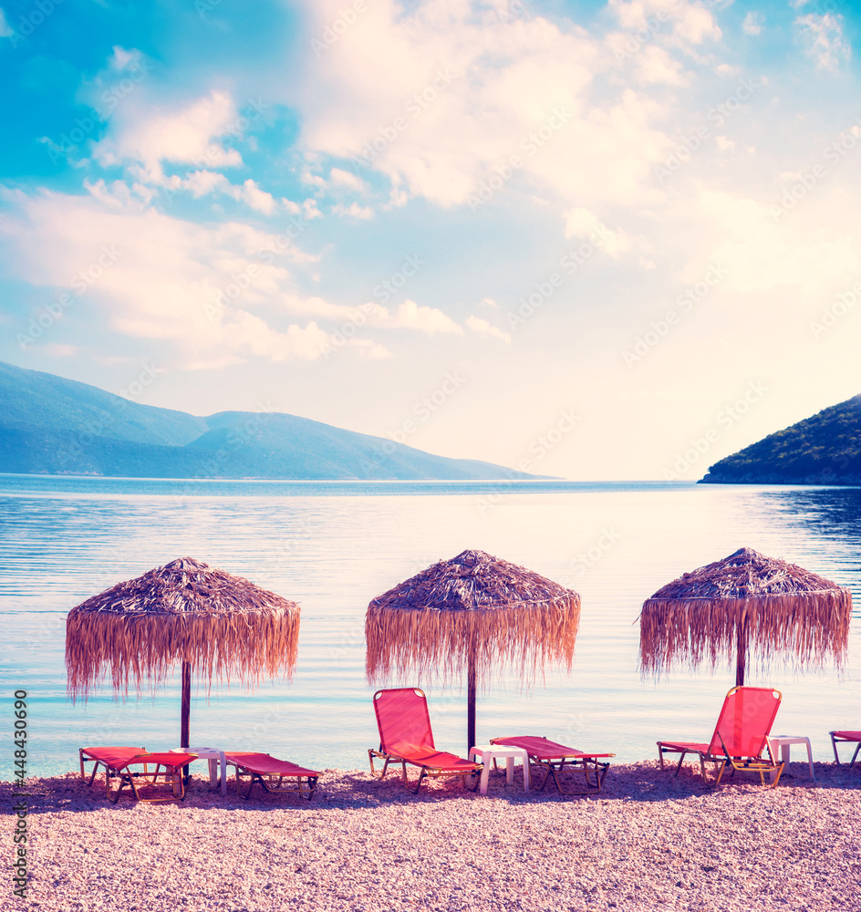 Fabulous landscape with umbrellas and orange sun beds on the seafront on Antisamos Beach on a sunny day on the coast of the Ionian Sea in Kefalonia, Greece. Amazing places. Tourist attractions.