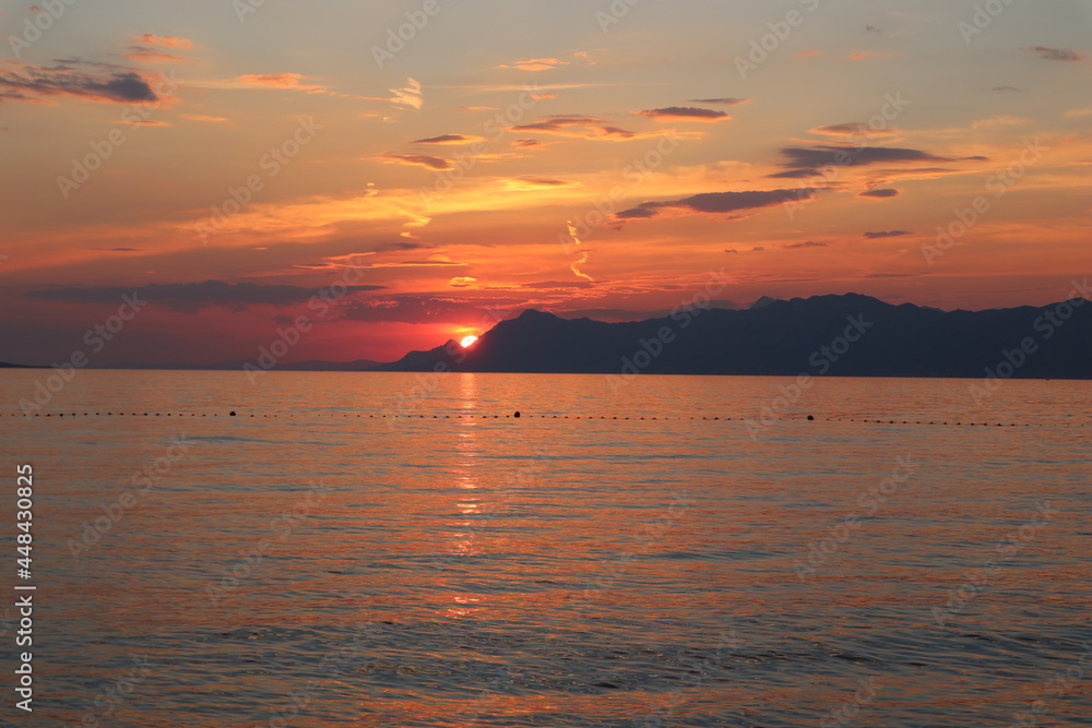 Bright colorful sunset on the beach, Croatia,Makarska. Seascape the sun sets behind the mountains on the sea coast, red-orange sky and sea on a summer evening