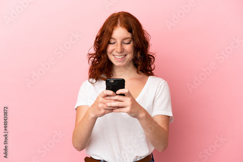Teenager reddish woman isolated on pink background sending a message or email with the mobile