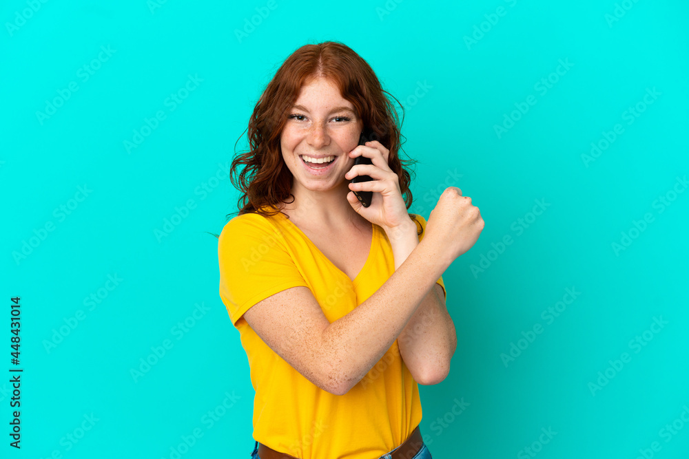 Teenager reddish woman using mobile phone isolated on blue background celebrating a victory Teenager reddish woman using mobile phone isolated on blue background celebrating a victory