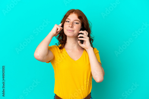 Teenager reddish woman using mobile phone isolated on blue background thinking an idea