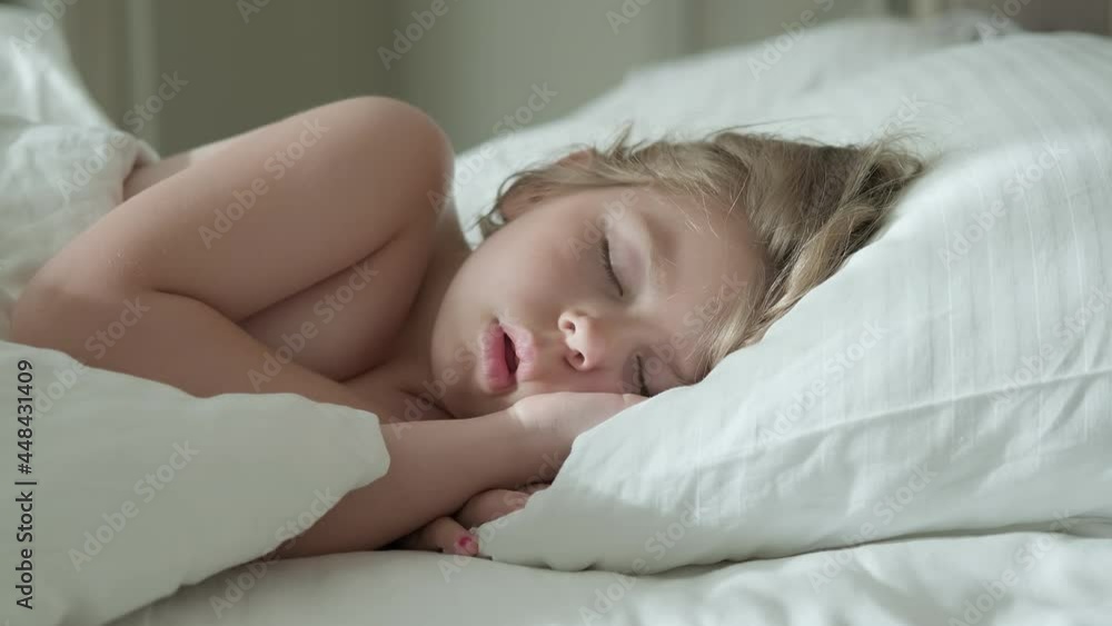 Peaceful little girl sleeping on bed in room. Bedtime rest. Carefree childhood. Sunny morning. Sleeping baby concept. 4K, UHD Peaceful little girl sleeping on bed in room. Bedtime rest. Carefree childhood. Sunny morning. Sleeping baby concept. 4K, UHD