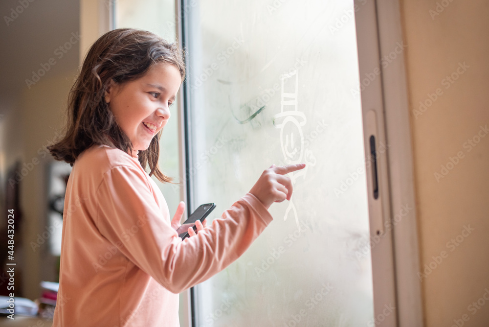 Niña jugango con la humedad de la puerta de vidrio por el frio dibujando un muñeco y sacandole una foto con el celular. Niña jugango con la humedad de la puerta de vidrio por el frio dibujando un muñeco y sacandole una foto con el celular.