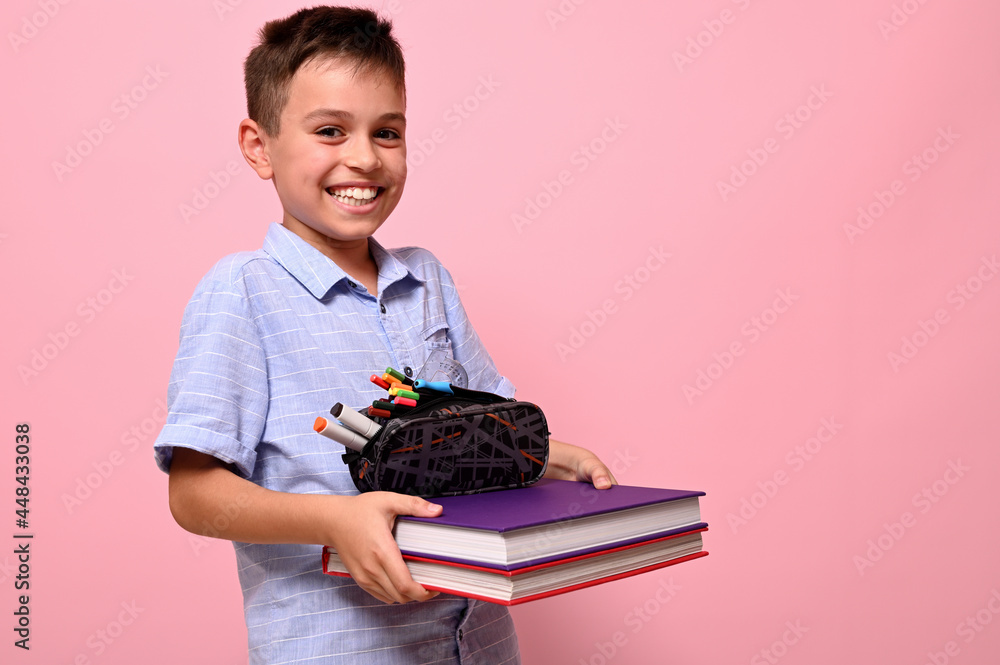 A smiling boy, student at school, holds books and pencil case in front ...