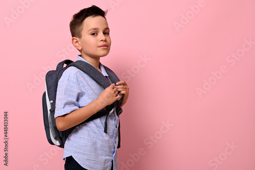 Side portrait of a schoolboy with a school bag on his back on pink background with copy space. Back to school concepts