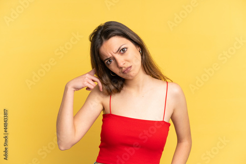 Young caucasian woman isolated on yellow background making the gesture of madness putting finger on the head