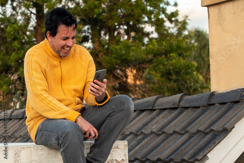Auto retrato de hombre blanco en el tejado en un dia de otoño con campera amarillo y un celular haciendo selfie luz natural.