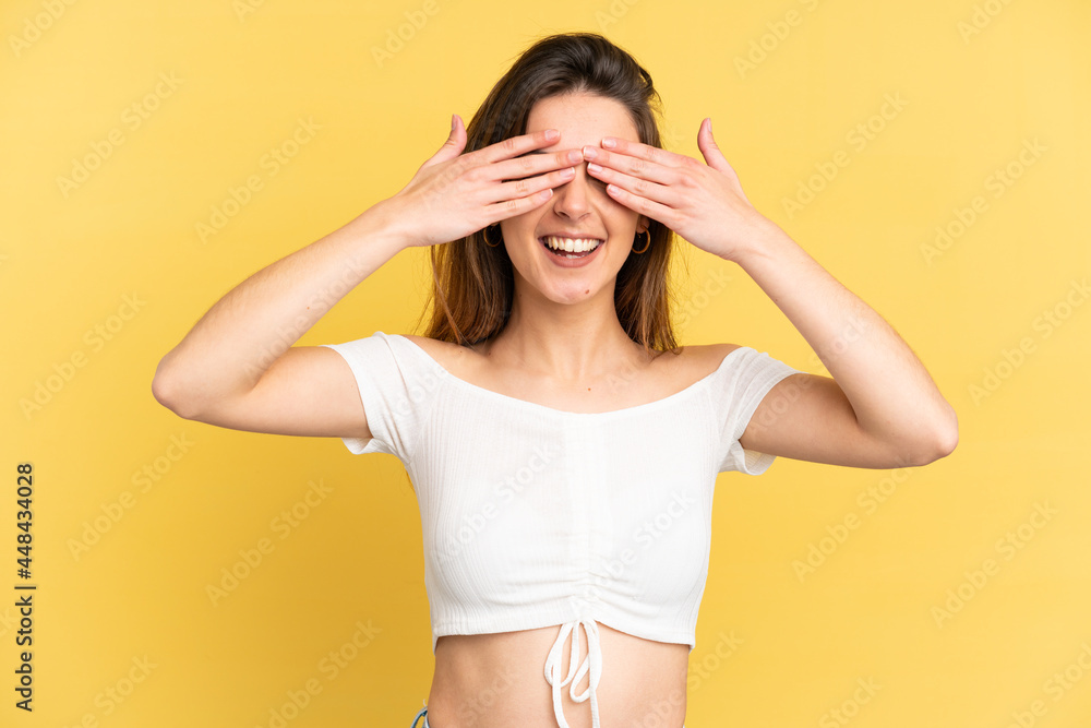 Young caucasian woman isolated on yellow background covering eyes by hands and smiling Young caucasian woman isolated on yellow background covering eyes by hands and smiling
