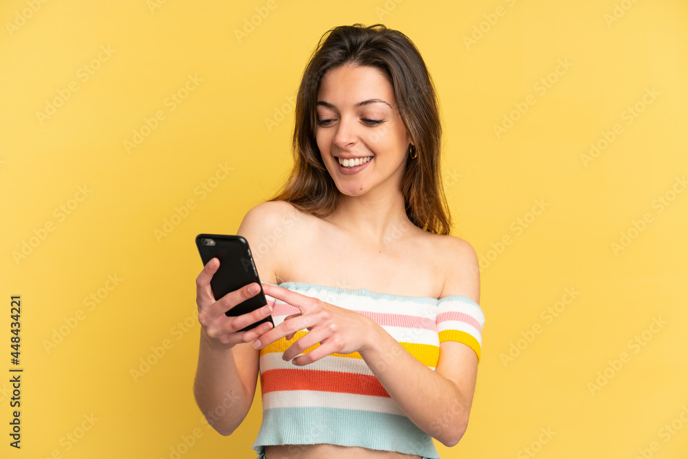 Young caucasian woman isolated on yellow background sending a message or email with the mobile Young caucasian woman isolated on yellow background sending a message or email with the mobile