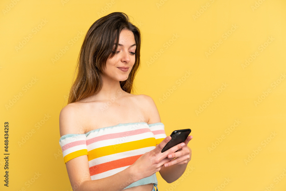 Young caucasian woman isolated on yellow background sending a message or email with the mobile Young caucasian woman isolated on yellow background sending a message or email with the mobile